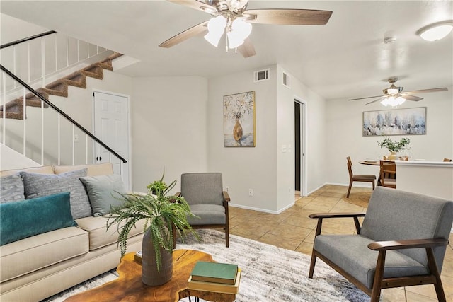 living room with light tile patterned floors, a ceiling fan, visible vents, stairs, and baseboards