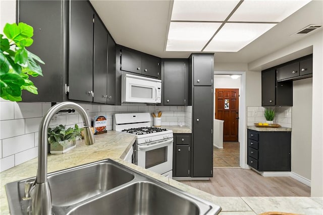 kitchen with light countertops, visible vents, a sink, white appliances, and dark cabinetry