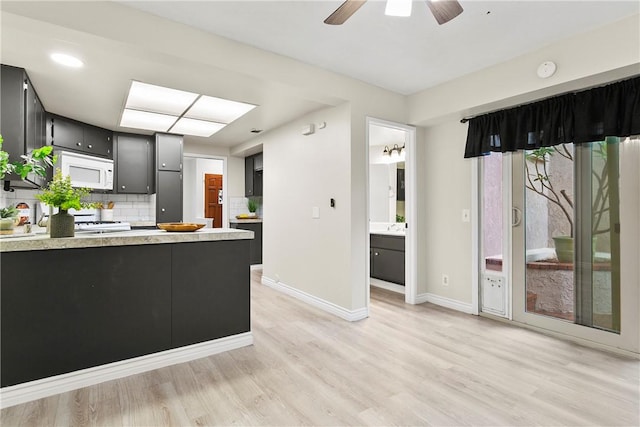 kitchen with white microwave, light wood-style flooring, light countertops, dark cabinetry, and backsplash