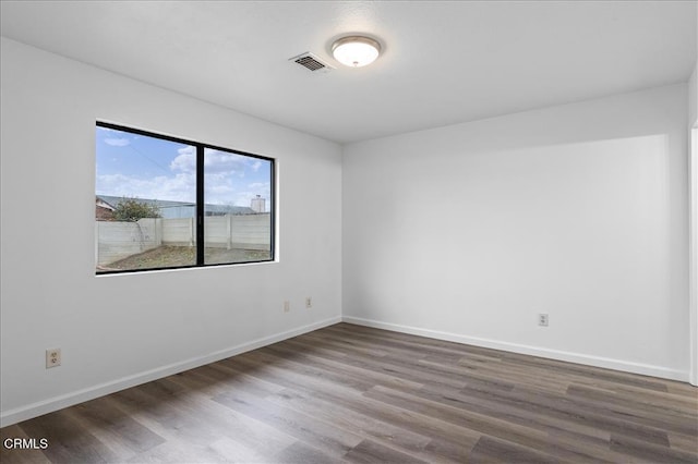 empty room featuring wood finished floors, visible vents, and baseboards