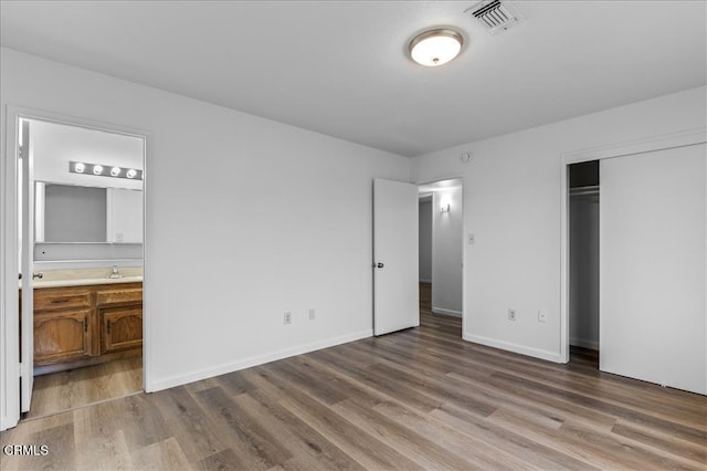 unfurnished bedroom featuring baseboards, visible vents, wood finished floors, ensuite bathroom, and a closet