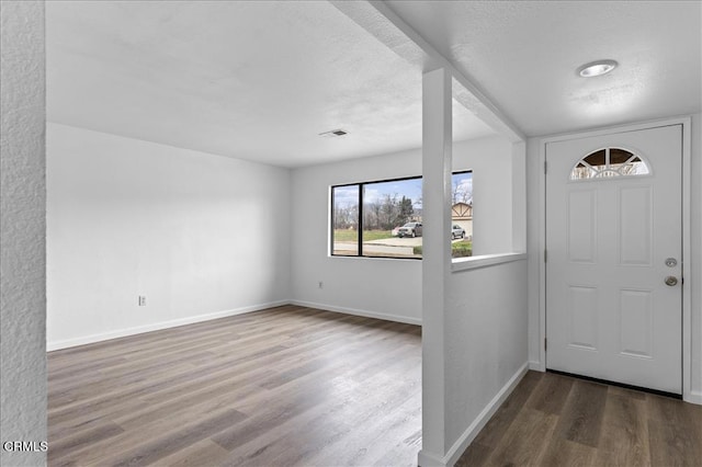 entrance foyer with a textured ceiling, wood finished floors, visible vents, and baseboards