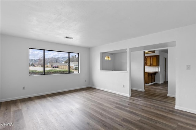 unfurnished room featuring baseboards, visible vents, dark wood finished floors, and a textured ceiling