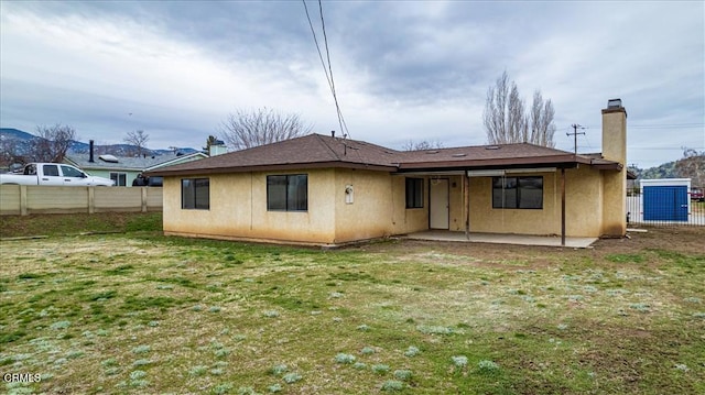 rear view of house featuring a yard, a patio area, fence, and stucco siding