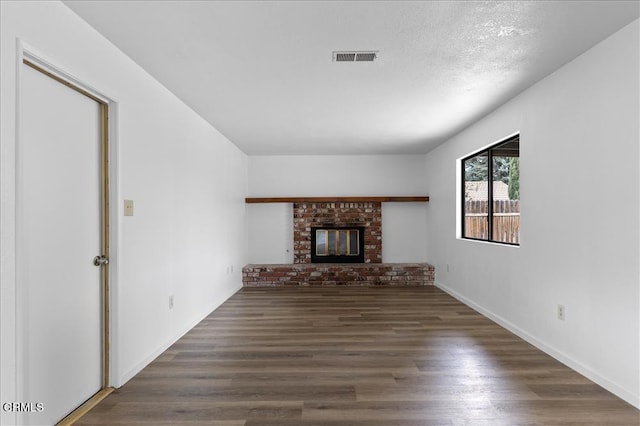 unfurnished living room with baseboards, visible vents, wood finished floors, a textured ceiling, and a brick fireplace