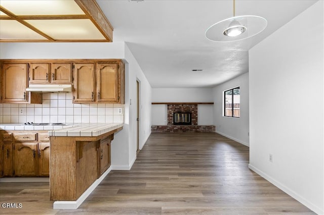 kitchen featuring tile counters, tasteful backsplash, open floor plan, light wood-type flooring, and under cabinet range hood