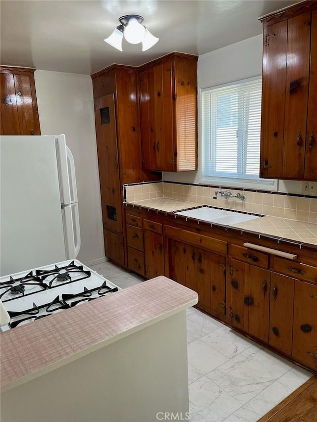 kitchen featuring tile countertops, marble finish floor, a sink, and freestanding refrigerator