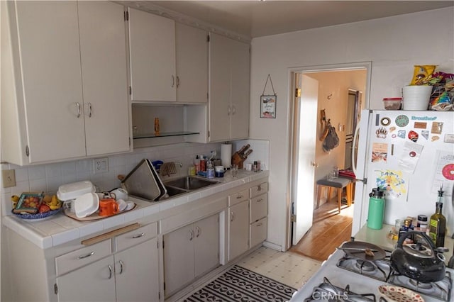 kitchen with light floors, tile counters, tasteful backsplash, freestanding refrigerator, and a sink