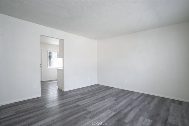 empty room featuring a textured ceiling, dark wood-style flooring, and baseboards