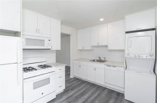 kitchen featuring light countertops, white cabinets, a sink, stacked washing maching and dryer, and white appliances