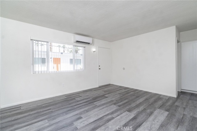 empty room featuring a wall mounted air conditioner, a textured ceiling, baseboards, and wood finished floors