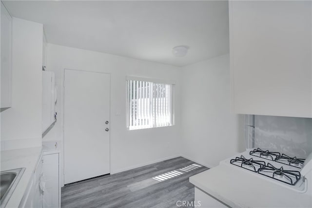 kitchen with light countertops, light wood-style floors, white cabinetry, a sink, and stovetop