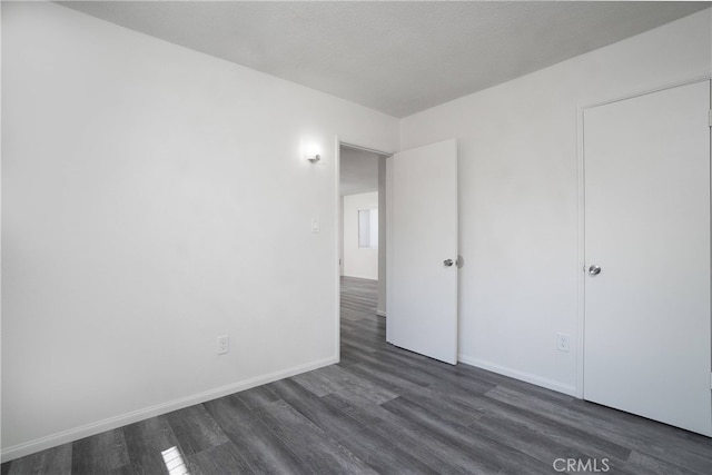 unfurnished bedroom with baseboards and dark wood finished floors