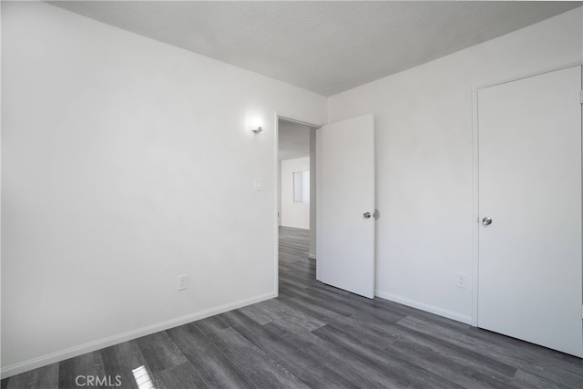 unfurnished bedroom with baseboards and dark wood-type flooring