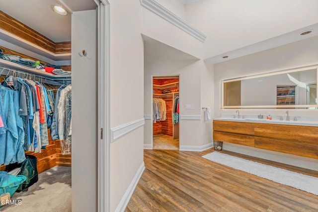 bathroom featuring wood finished floors, a walk in closet, baseboards, and double vanity