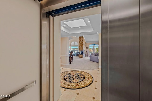 hallway featuring carpet, a tray ceiling, recessed lighting, a skylight, and tile patterned floors