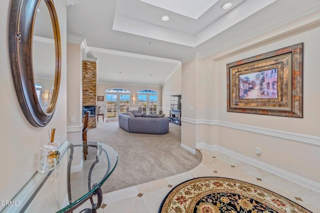 carpeted foyer featuring a raised ceiling, a skylight, a fireplace, crown molding, and baseboards