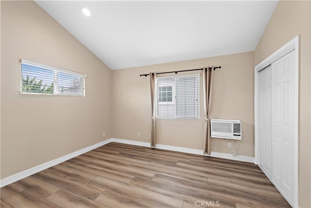 unfurnished bedroom with wood finished floors, baseboards, vaulted ceiling, an AC wall unit, and a closet