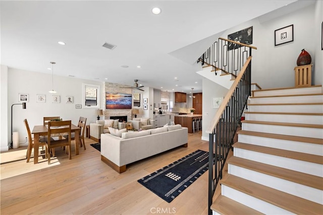 living area with light wood-style floors, recessed lighting, a fireplace, and stairway