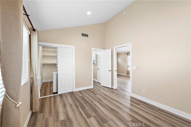 unfurnished bedroom featuring high vaulted ceiling, visible vents, baseboards, and wood finished floors