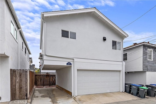 exterior space featuring concrete driveway, an attached garage, fence, and stucco siding