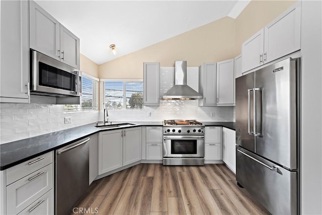 kitchen featuring light wood finished floors, high end appliances, vaulted ceiling, a sink, and wall chimney exhaust hood