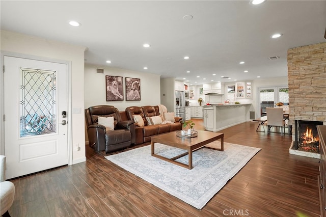 living room with recessed lighting, visible vents, dark wood-type flooring, a stone fireplace, and baseboards