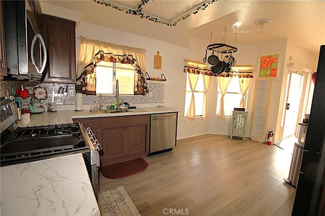 kitchen with appliances with stainless steel finishes, a sink, light wood-style flooring, and decorative backsplash