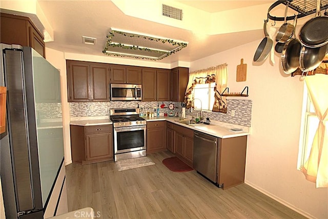 kitchen featuring stainless steel appliances, visible vents, decorative backsplash, a sink, and light wood-type flooring