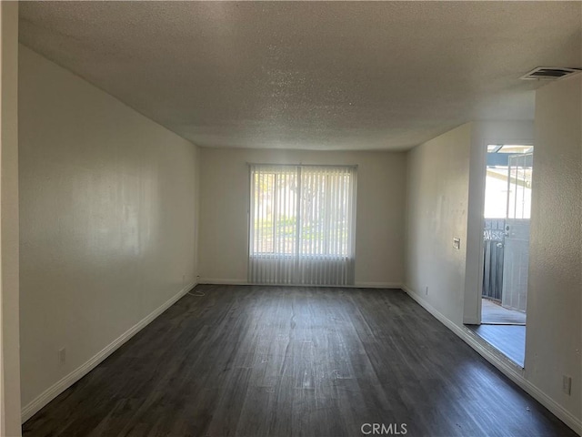 spare room with a textured ceiling, dark wood-type flooring, plenty of natural light, and visible vents