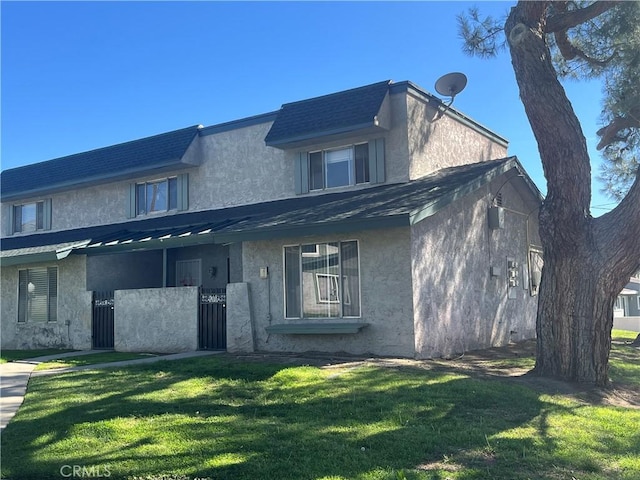 multi unit property with stucco siding, a shingled roof, mansard roof, and a front yard