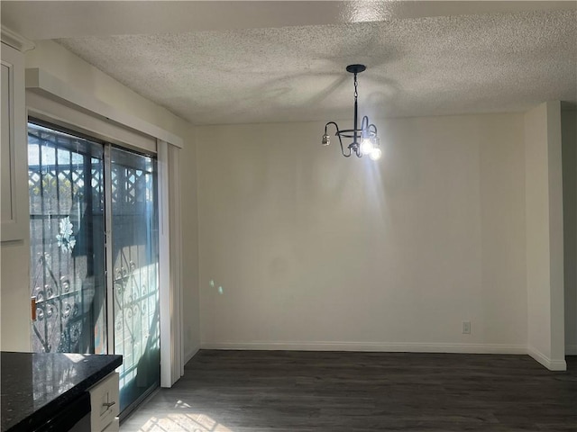 unfurnished dining area featuring a notable chandelier, a textured ceiling, baseboards, and wood finished floors