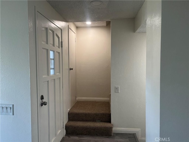 stairway with a textured ceiling, a textured wall, wood finished floors, and baseboards