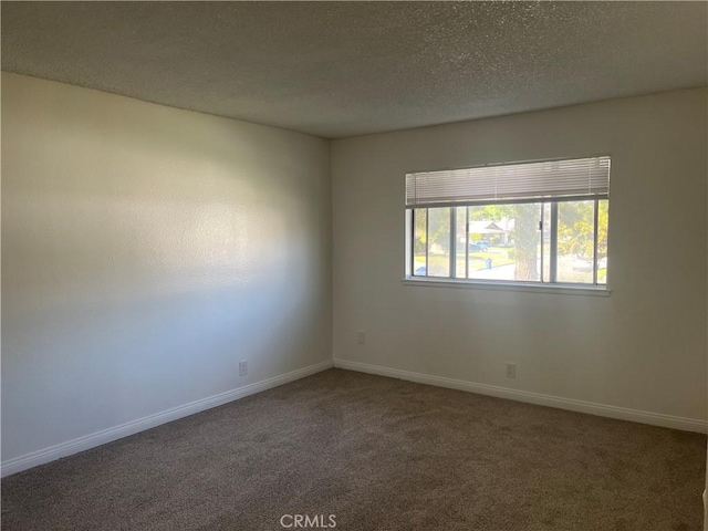 carpeted spare room featuring a textured ceiling and baseboards