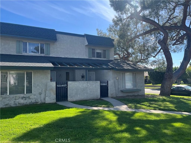 multi unit property featuring a shingled roof, a front yard, and stucco siding