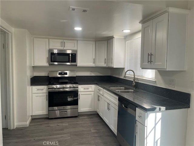 kitchen featuring appliances with stainless steel finishes, dark countertops, a sink, and visible vents