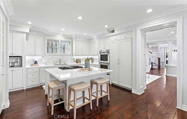 kitchen featuring appliances with stainless steel finishes, white cabinetry, a sink, a kitchen island, and ornate columns