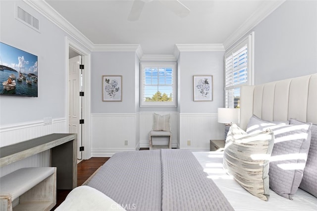 bedroom featuring visible vents, a ceiling fan, wainscoting, wood finished floors, and crown molding