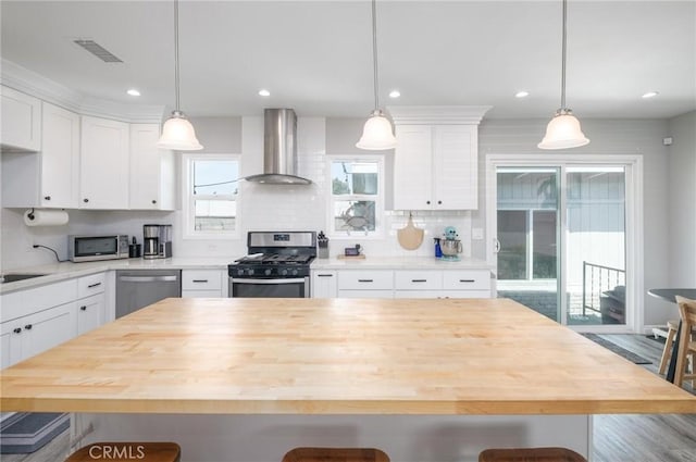 kitchen with a kitchen bar, visible vents, appliances with stainless steel finishes, white cabinetry, and wall chimney exhaust hood