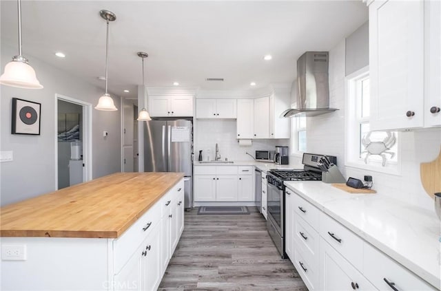 kitchen with stainless steel appliances, white cabinetry, wooden counters, wall chimney exhaust hood, and tasteful backsplash