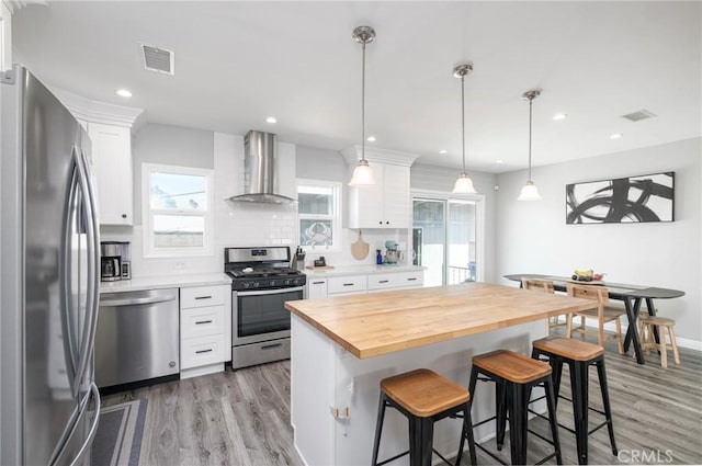 kitchen featuring a breakfast bar, wall chimney exhaust hood, visible vents, and stainless steel appliances