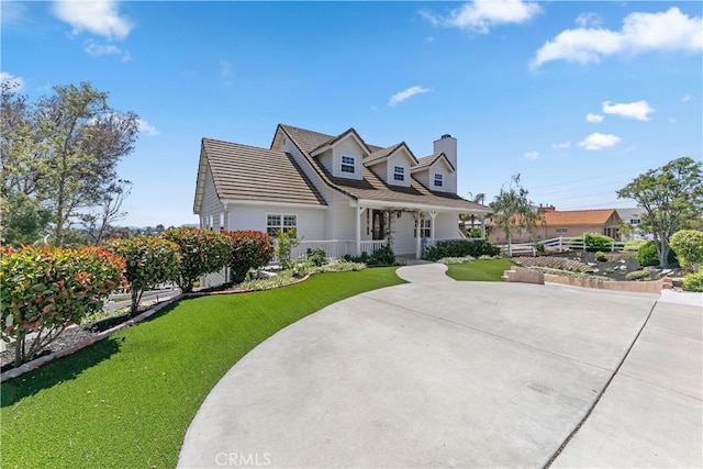 cape cod house featuring a front yard, driveway, and a chimney