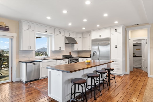 kitchen with a breakfast bar area, stainless steel appliances, a sink, wood counters, and under cabinet range hood