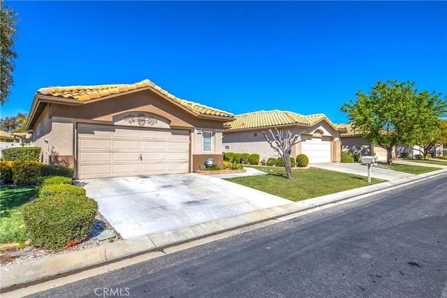 mediterranean / spanish-style house featuring stucco siding, a garage, driveway, a tiled roof, and a front lawn