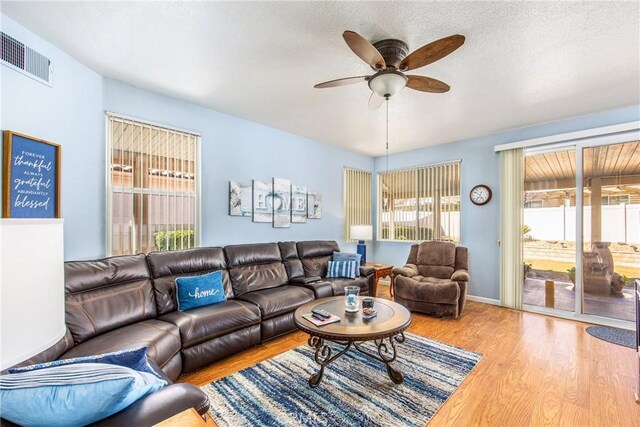 living area featuring a ceiling fan, a textured ceiling, visible vents, and wood finished floors