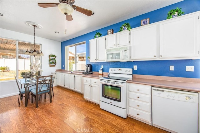 kitchen with white appliances, white cabinetry, light wood-style floors, and decorative light fixtures