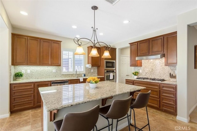 kitchen with appliances with stainless steel finishes, a center island, brown cabinetry, and under cabinet range hood