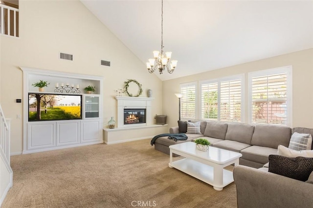 carpeted living area with high vaulted ceiling, a glass covered fireplace, visible vents, and an inviting chandelier