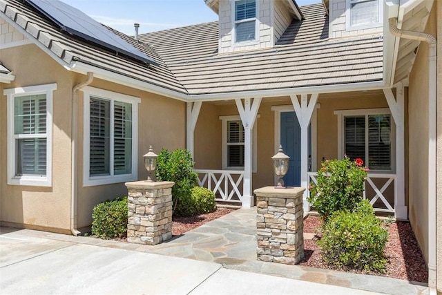 property entrance with covered porch, solar panels, and stucco siding