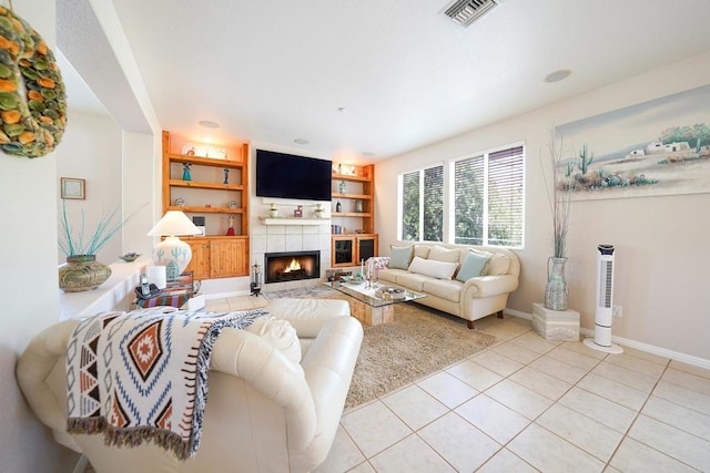 living room featuring built in features, light tile patterned floors, visible vents, a tile fireplace, and baseboards